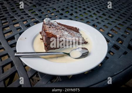 Ein Stück Schokoladenkuchen tropft in Sahne auf einem weißen Teller. Stockfoto