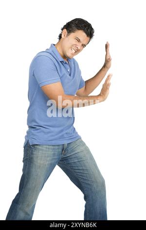 Ein starker, kämpfender latino-Mann in lässiger blauer Kleidung mit ausgestreckten Armen verteidigt, drängt und drückt gegen imaginäre Einlegeobjekte, die in Berührung kommen Stockfoto