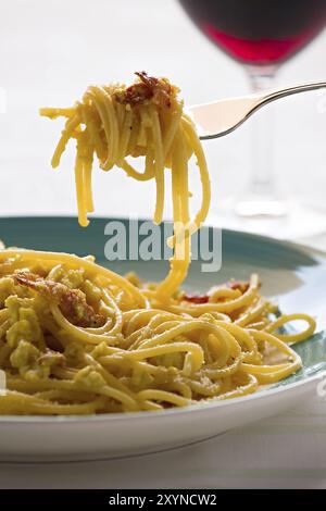 Nahaufnahme von Spaghetti Carbonara auf Gabel mit Ei, Speck und Käse über einen Tisch mit Rotwein Glas Stockfoto