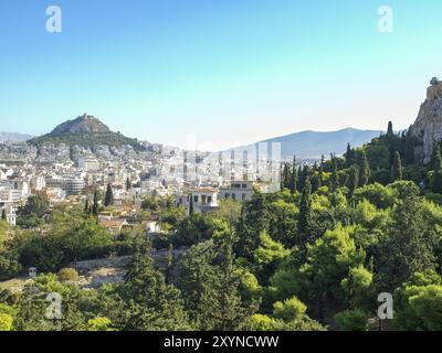 Stadtpanorama mit einem grünen Hügel, vielen Bäumen und Häusern, eingebettet zwischen Bergen unter klarem Himmel, athen, griechenland Stockfoto