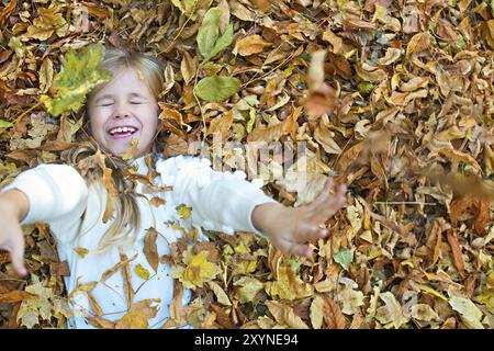 Kind spielt im Herbst Park. Kind werfen gelbe und rote Blätter. Kleines Mädchen mit Eiche und Ahorn Blatt. Herbst Laub. Spaß im Freien im Herbst. Schooler chi Stockfoto