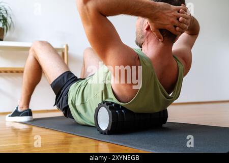 Männlicher Athlet, der Fitnessübungen mit Schaumstoffrolle, Heimtraining, Körperpflege macht. Stockfoto