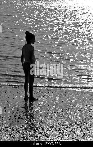 Silhouette eines Mädchens, das in der Sonne am Meer steht Stockfoto