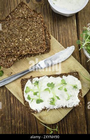 Scheibe Vollkornbrot mit frisch geschnittener Kresse und Frischkäse auf einem alten Holztisch (selektiver Fokus, Nahaufnahme) Stockfoto