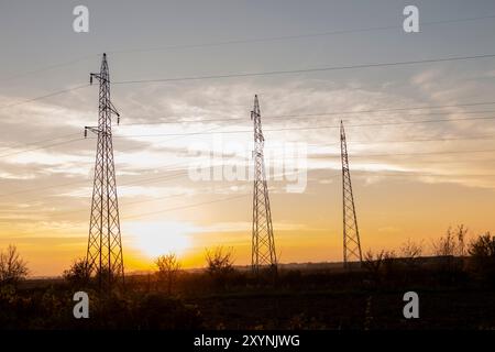 Hochspannungsleitungen bei Sonnenuntergang. In Zukunft - Elektrizitätsknappheit. Wegen der hohen Preise haben verzweifelte Menschen kein Geld für Strom Stockfoto