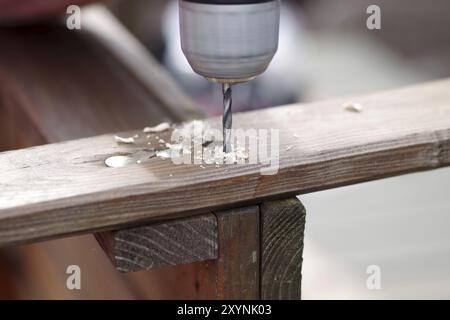 Holzbohrer, Holzspäne, Loch, Brett, DIY, Nahaufnahme eines Akkuschraubers mit Holzbohrer. Ein Loch wird in das Holz gebohrt, um ein altes Holz zu erhalten Stockfoto