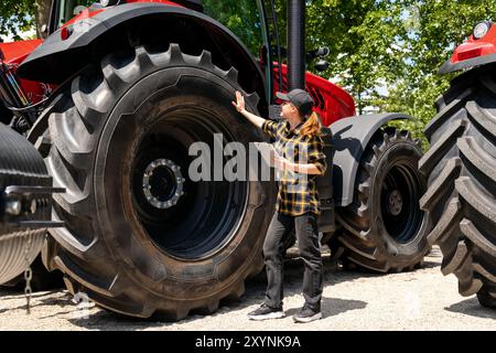 Eine Frau mit einem digitalen Tablet in der Hand berührt ein großes Rad einer Bau- oder Landmaschine. AG-Gerätehändler. Stockfoto