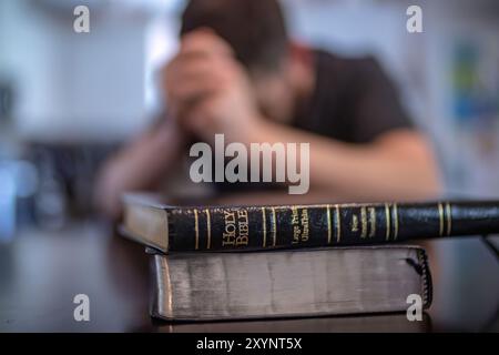 Nahaufnahme der Lederbibel mit Worten aus der Heiligen Bibel in fokussierter Sprache, Mann betend im Hintergrund von Bokeh Stockfoto