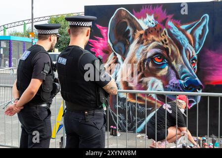 Southend on Sea, Essex, Großbritannien. 30. August 2024. Southend feiert seinen Stadtstatus mit dem City Jam Event. Mehr als 200 lokale, nationale und internationale Straßenkünstler zeigen ihr Können an verschiedenen Orten im Stadtzentrum. Einige temporäre Mauern wurden errichtet, aber die Künstler dekorieren auch die Seiten von Gebäuden, Häusern und anderen dauerhaften Bauten. Künstler können an den Wandgemälden in den Straßen und Grundstücken arbeiten. Polizeibeamte beobachten Stockfoto