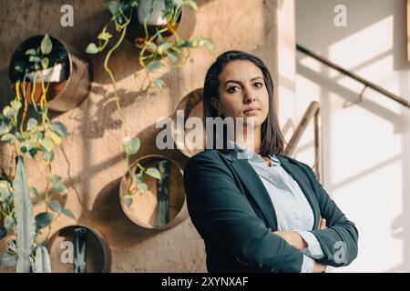 Geschäftsfrau steht mit überkreuzten Armen in einem modernen Bürogebäude mit Pflanzen Stockfoto
