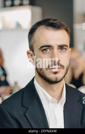 Junger Geschäftsmann mit einem ordentlichen Bart, der eine schwarze Anzugsjacke über einem weißen Hemd trägt Stockfoto