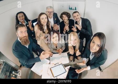 Verschiedene Gruppen von Geschäftsleuten applaudieren, während sie an einem Tisch mit Papierkram stehen Stockfoto