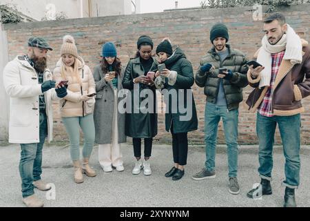 Gruppe junger Menschen, die im Stadtzentrum Smartphones benutzen und Winterkleidung tragen Stockfoto