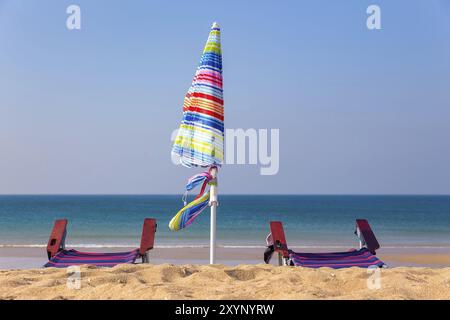 Farbenfroher Sonnenschirm mit Liegen am Strand mit blauem Meer Stockfoto