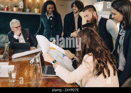 Verschiedene Teams von Geschäftsleuten versammeln sich an einem Tisch, analysieren Blaupausen und diskutieren ein Projekt Stockfoto