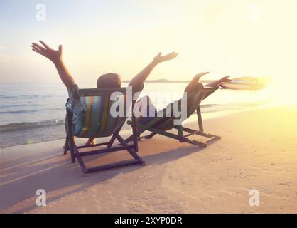 Glückliches Paar, das bei Sonnenuntergang am Strand von Koh Samet auf Sonnenliegen sitzt, Thailand, Asien Stockfoto