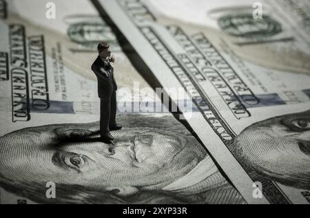 Miniaturfigur Geschäftsmann mit 100-Dollar-Banknote auf dem Hintergrund. Konzept Stockfoto