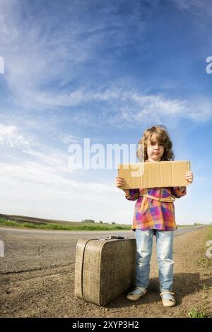 Einsames Mädchen mit Koffer, der auf der Straße steht und Papier hält, mit Kopierraum in den Händen Stockfoto