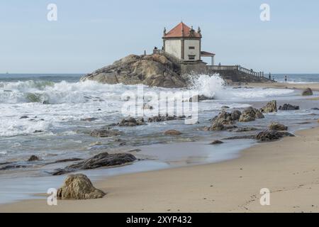 Wellen, Surfen, Sandstrand und Wahrzeichen Capela do Senhor da Pedra, historische Kapelle auf einem Felsen am Praia do Senhor da Pedra, Gulpilhares, Vila Nova de Gaia Stockfoto