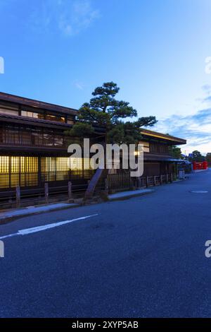 Die moderne Straße verläuft vor einem traditionellen japanischen Holzhaus, das in der Dämmerung beleuchtet wird, vorbei an der Naka-Bashi-Brücke im historischen alten Viertel von Hida-Takay Stockfoto