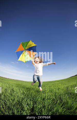 Glückliches Kind im grünen Feld gegen blauen Himmel springen. Sommer Urlaub Konzept Stockfoto