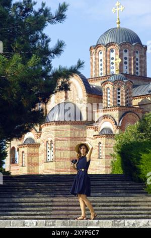 Eine Frau steht mit einer DSLR-Kamera vor einer Kirche. Weibliche Touristin im Kloster Hercegovacka Gracanica (Trebinje, Bosnien und Herzegowina). Stockfoto