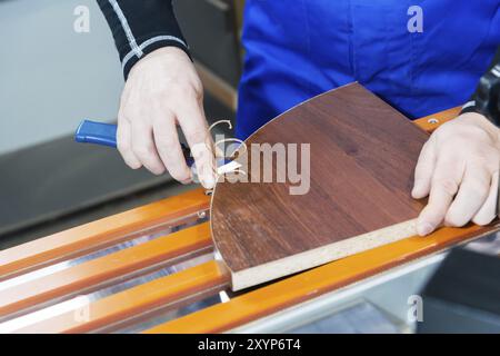 Ein professioneller Zimmermann verarbeitet die Kunststoffkanten der Arbeitsplatte mit einem Messerkantenschnitt. Das Konzept der Möbelproduktion Stockfoto