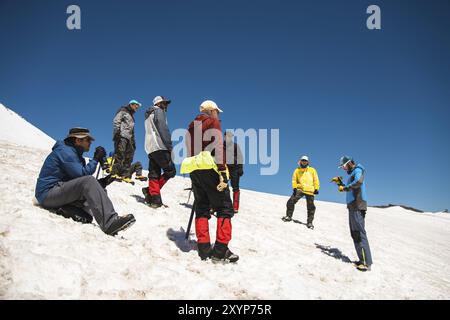 Training zum Korrigieren des Rutschens an Hanglagen oder Gletschern mit Hilfe einer Eispistole. Ein junger Reiseleiter mit Bart erklärt seiner Gruppe, wie man das richtig verlangsamt Stockfoto