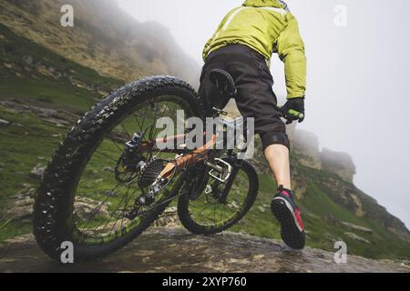 Beine des Radfahrers und Hinterrad Nahaufnahme des hinteren MTB-Bikes in den Bergen vor dem Hintergrund von Felsen bei nebeliger Witterung. Das Konzept der extremen spor Stockfoto