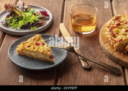 Ein französisches Abendessen. Eine Scheibe einer Quiche Lorraine mit mesclun Blätter und weißen Wein auf einem dunklen Holzmöbeln im Landhausstil Hintergrund Stockfoto