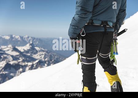 Nahaufnahme Ein junger Kletterer hält in der Hand eine Eisaxt, die auf dem Gipfel hoch in den Bergen vor dem Hintergrund des schneebedeckten Kaukasiens steht Stockfoto