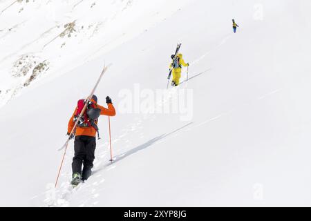 Zwei Ski Freerider klettern die Piste in Tiefschneepulver, wobei die Ausrüstung auf der Rückseite auf dem Rucksack befestigt ist. Das Konzept des Winterextremen Sports Stockfoto