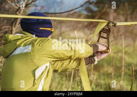 Die Nahhand Eines Mannes passt das Slacklining der Ausrüstung an, bevor er verrückte Slackliner-Tricks ausführt und in einem Park im nat auf einem Slacklin läuft Stockfoto