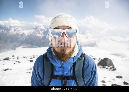 Porträt eines bärtigen Reiseleiters mit Hut und Sonnenbrille vor dem Hintergrund schneebedeckter Berge Stockfoto