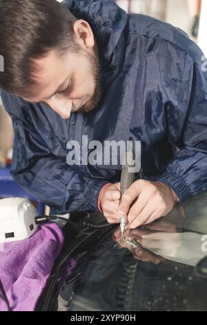 Nahaufnahme von Autoverglasungsarbeitern, die eine Windschutzscheibe oder Windschutzscheibe eines Autos an einer Werkstattwerkstatt reparieren und reparieren. Bohren Sie das Glas für die Reparatur Stockfoto