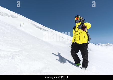 Skifahrer, der auf einer Piste steht. Mann in einem leichten Anzug, Helm und Maske beim Skifahren ist Ski fahren. Im Hintergrund schneebedeckte Berge, Skifahrer, Kaukasus MoU Stockfoto