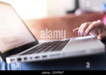 Mädchen mit violetten Fingernägeln benutzt ihren Laptop zu Hause auf der Couch Stockfoto