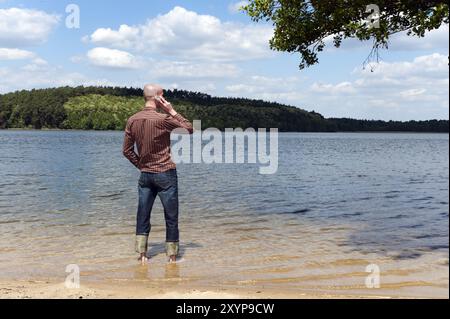 Junger Mann, der in einem See steht und am Telefon spricht Stockfoto