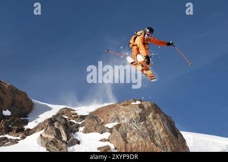 Ein professioneller Skifahrer macht einen Sprung von einer hohen Klippe gegen den blauen Himmel und hinterlässt eine Spur aus Schneepulver in den Bergen. Foto von den Pisten o Stockfoto