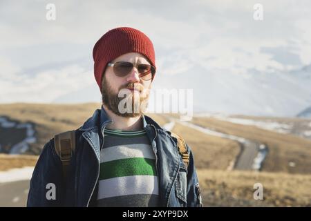 Modeporträt eines bärtigen jungen Hipster-Mannes mit Sonnenbrille, Rucksack und Hut auf einem Hintergrund mit Copyspase in den Bergen bei Sonnenuntergang, Eine Co Stockfoto