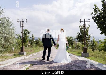 Porträt eines netten Paares, das an einem Hochzeitstag auf Hochzeitsreise war, mit einem Blumenstrauß in den Händen, der sich gegenseitig lachend und lächelnd vor einer grünen Gasse ansah Stockfoto