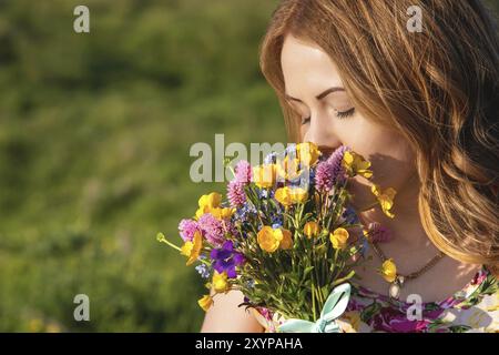 Nahporträt eines rustikalen Mädchens. Ein Mädchen in einem bunten Kleid hält einen Blumenstrauß. Schnüffelnde Blumen Stockfoto