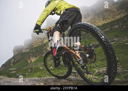 Beine des Radfahrers und Hinterrad Nahaufnahme des hinteren MTB-Bikes in den Bergen vor dem Hintergrund von Felsen bei nebeliger Witterung. Das Konzept der extremen spor Stockfoto