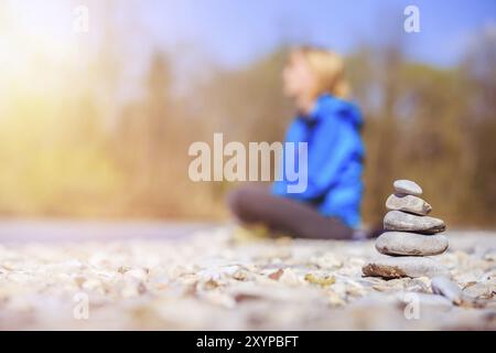 Cairn an einem Kiesstrand, meditierende Frau im Hintergrund. Morgensonne Stockfoto