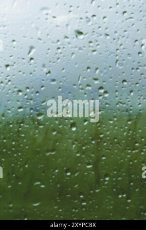 Natürlicher Hintergrund fällt auf beiden Seiten des Glases aus dem Regen und aus der nebelnden abstrakten Ansicht, Regentropfen auf das blaue Glas und die Unschärfe Stockfoto