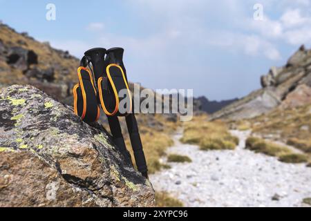 Professionelle Sticks zum Besteigen eines Berges in der Nähe eines Steines auf einem hohen Bergweg vor blauem Himmel und weißen Wolken. Das Konzept der aktiven Erholung Stockfoto