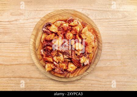 Pulpo a la gallega, ein Tintenfisch mit gekochten Kartoffeln und Paprika, ein typisch spanisches galizisches Gericht, auf einem traditionellen Holzteller, von oben geschossen Stockfoto