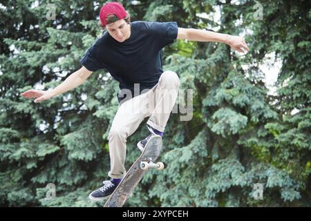 Der langhaarige Skater-Teenager in T-Shirt und Sneakermütze springt die ollie vor dem Hintergrund eines stürmischen Himmels durch die Stadt Stockfoto