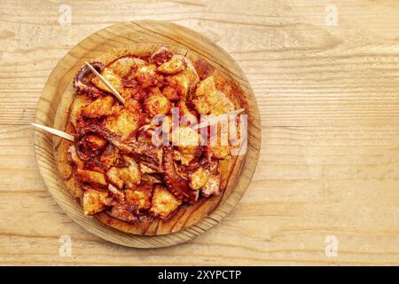 Pulpo a la gallega, ein Tintenfisch mit gekochten Kartoffeln und Paprika, ein typisch spanisches galizisches Gericht, auf einem traditionellen Holzteller, von oben auf einem geschossen Stockfoto