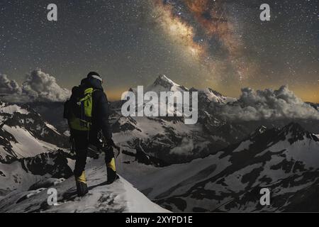 Nachtfoto. Professioneller Bergsteiger, voll ausgestattet und mit einem Rucksack auf den Schultern und einer Eispistole in den Händen steht auf der mou Stockfoto